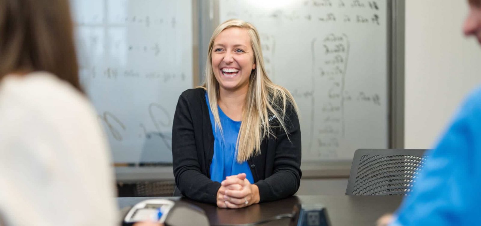 A smiling woman is sitting in a conference room and being interviewed by two people